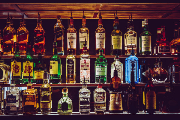 Scaffale di un bar con una vasta selezione di bottiglie di liquori e whisky disposte su più ripiani